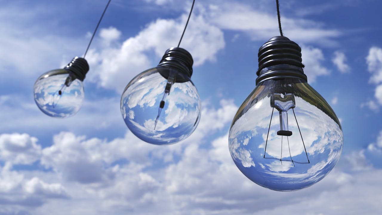Ampoules suspendues reflétant un ciel bleu avec des nuages, symbolisant l’énergie propre et naturelle